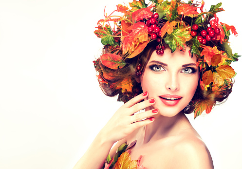 Autumn leaves and red berry in wreath on model head. Autumn style, bright makeup, red manicure and lipstick.