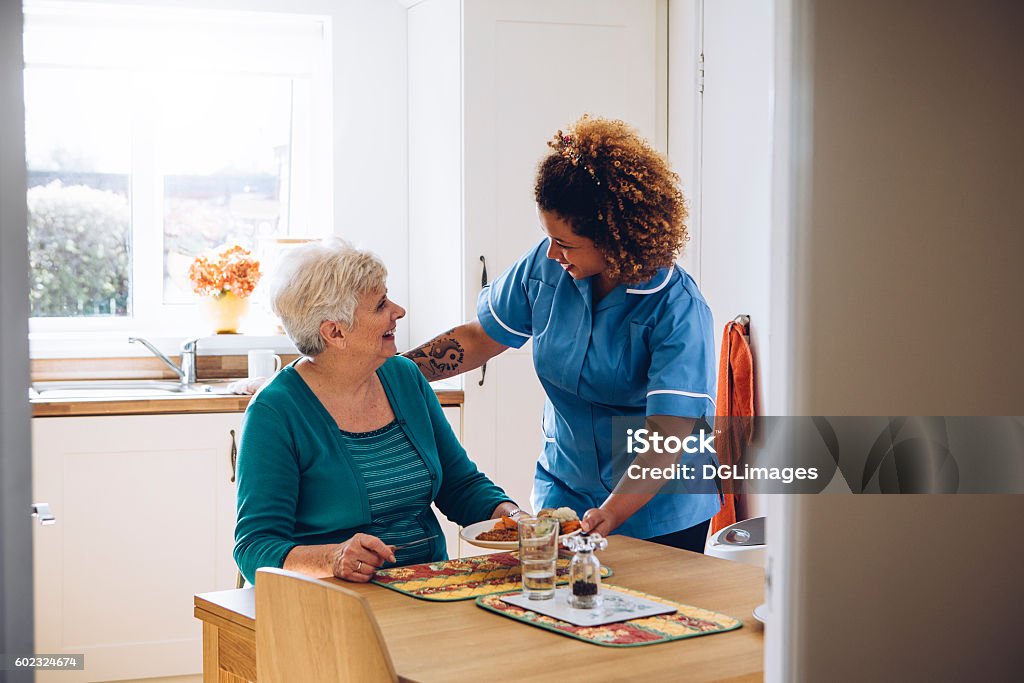 It's Dinner Time! Care worker giving an old lady her dinner in her home. Home Caregiver Stock Photo