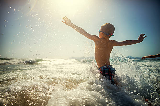 little boy playing and splashing in sea waves - child beach playing sun imagens e fotografias de stock