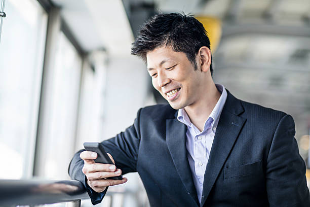 happy japanese businessman looking at his phone at the station - rush hour commuter on the phone tokyo prefecture imagens e fotografias de stock