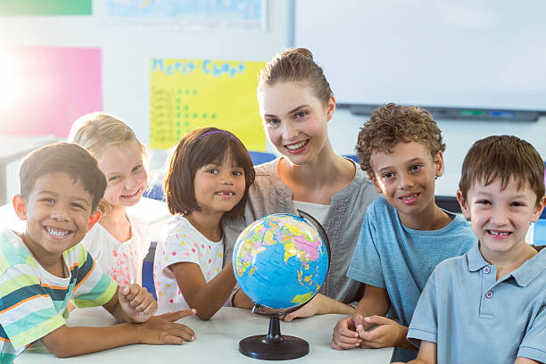istock Smiling teacher and schoolchildren with globe on table 602326372