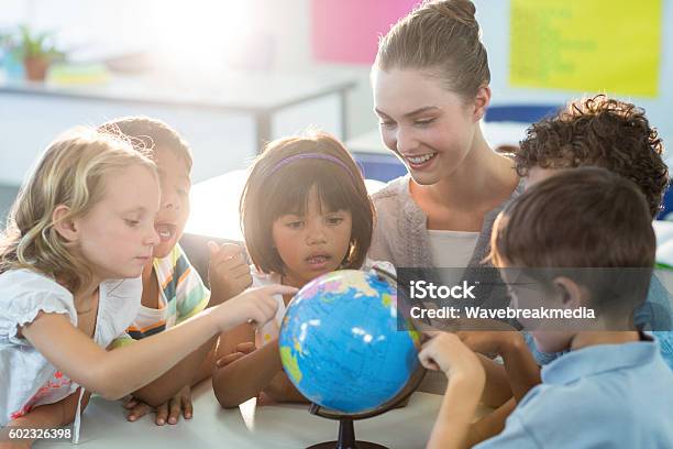 Teacher Looking At Schoolchildren Touching Globe Stock Photo - Download Image Now - Preschool, Globe - Navigational Equipment, Teacher