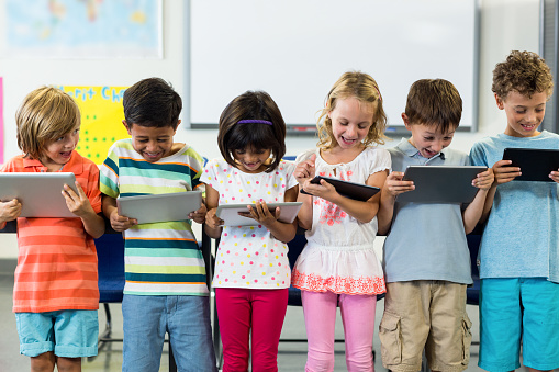 Smiling schoolchildren using digital tablets in classroom