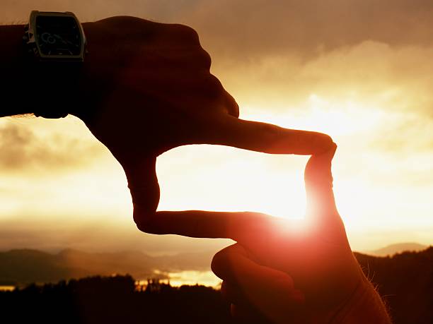 istock Hands with watch making frame. Dark misty landscape within daybreak. 602327390