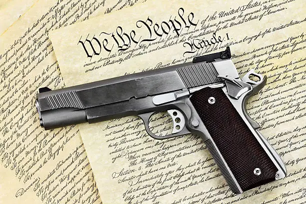 Handgun lying over a copy of the United States constitution with the words "We the People" visible.