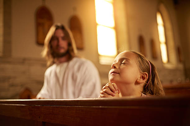 Cropped shot of a little girl praying in a church while Jesus watches over her