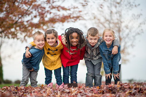 A multi-ethnic group of elementary age children are playing outside on a fall day. They are standing in a row and are smiling while looking at the camera.