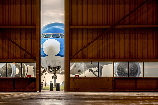Blue airplane in front of half opened door to hangar