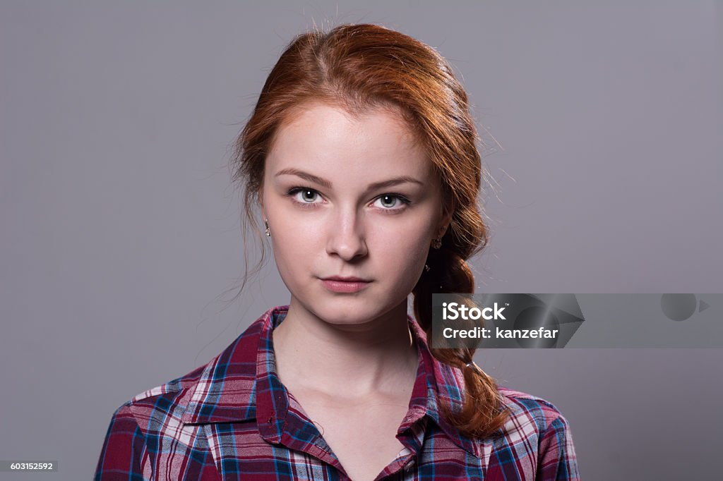 Serious girl looking at the camera Serious girl looking at the camera. Close-up portrait of a young woman in a checkered shirt on a gray background Teenager Stock Photo