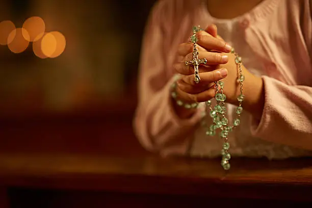 Cropped shot of an unidentifiable little girl praying while holding a rosary in church