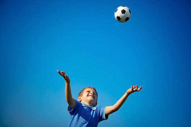 Happy boy playing ball Happy boy playing ball, cute little child catching ball over blue sky background, playing football in sunny summer day, happy healthy childhood running to catch the train stock pictures, royalty-free photos & images