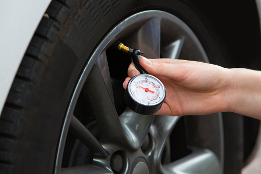 Primer plano de la mujer que comprueba la presión de los neumáticos del coche con el medidor photo