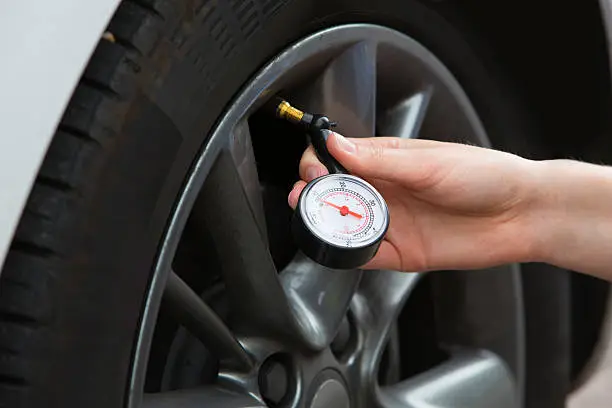 Close-Up Of Woman Checking Car Tyre Pressure With Gauge