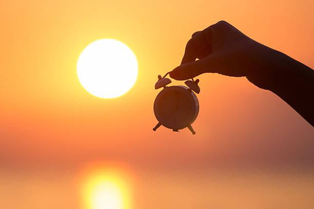 Female hand holding alarm clock at sunrise