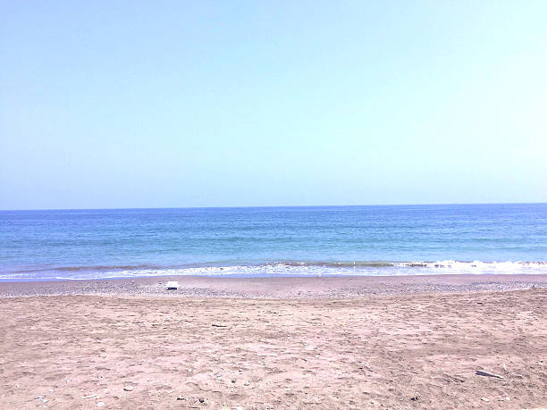 A peaceful scene of a sandy beach with gentle ocean waves rolling in under a clear blue sky. The image captures the serene beauty of the coastline, perfect for conveying relaxation, nature, and the simplicity of the seaside environment.