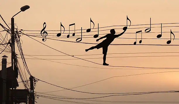 Sillouthe of a man putting music notes on wires . Concept of a crazy composer