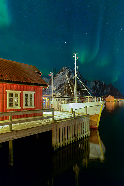 Northern lights over Svolvaer harbour in the Lofoten, Norway Northern Lights, polar light or Aurora Borealis in the night sky over the port of Svolvaer in the Lofoten in Nordland Norway. A fishing boat is moored in front of a cabin. harbor of svolvaer in winter lofoten islands norway stock pictures, royalty-free photos & images