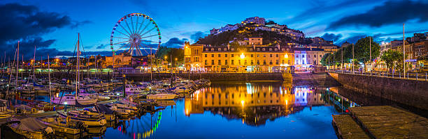 Devon Torquay harbour marina illuminated at sunset panorama Torbay UK The hotels and villas, quayside shops, pubs and restaurants of Torquay overlooking the harbour illuminated at dusk. devon stock pictures, royalty-free photos & images