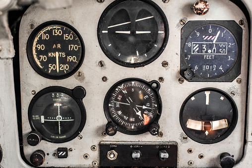 A retro aircraft control board, with a  mix of controls, switches, levers and dials.   Grey painted background.