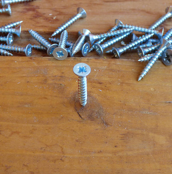 istock Screw in wooden board with fallen screws behind 603181204