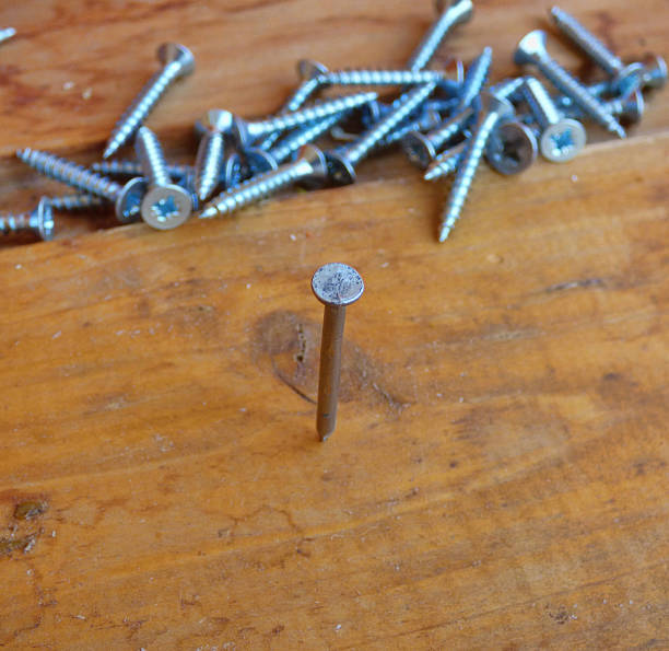 istock Nail hammered in board with fallen screws behind. Soft focus. 603181274