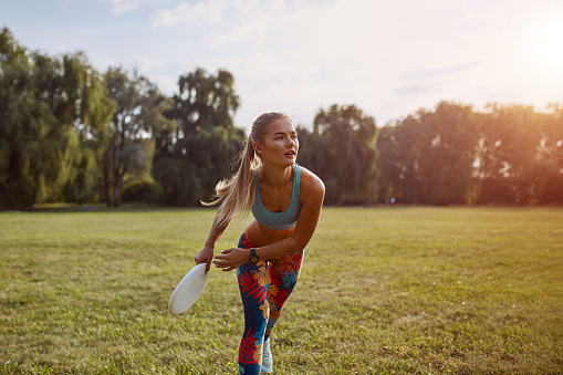 Young athletic girl playing frisbee in the park. Professional player. Sport concept