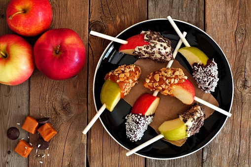 Plate of mixed sweet caramel and chocolate dipped apple slices, overhead scene on rustic wood