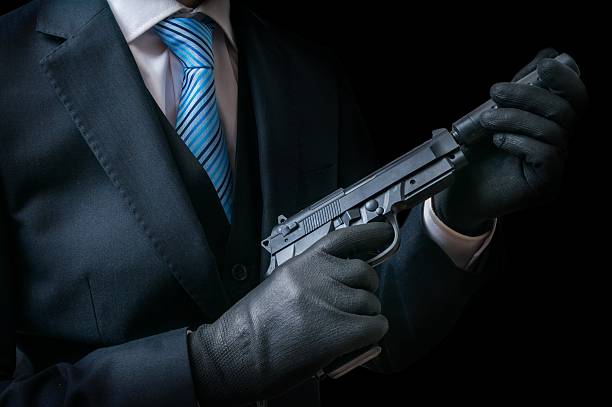 istock Mafia man holds pistol with silencer in hands. Low key. 603186382