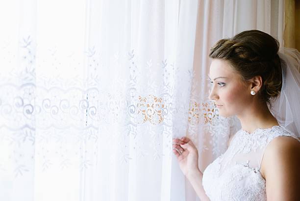 istock Young bride in white dress looking out the window. 603187818