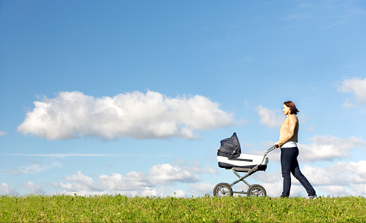 Young mother running while pushing a stroller on meadow