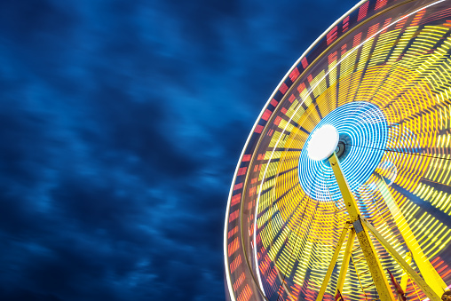 A ferris wheel is full of colour and motion under a canopy of moody clouds.