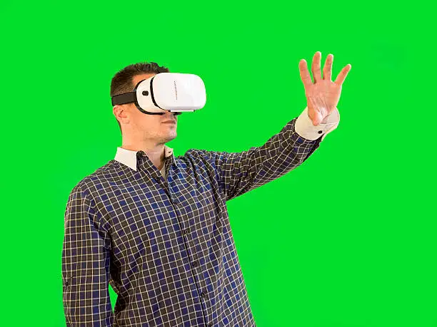 Guy holding hand out in front of green screen with VR glasses on