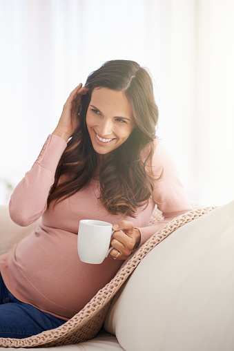 Shot of a pregnant woman having a warm beverage and relaxing at home