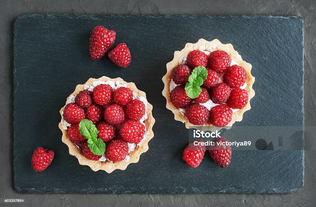 Tartlets with raspberries Tartlets with raspberries on a slate board background Tart - Dessert Stock Photo