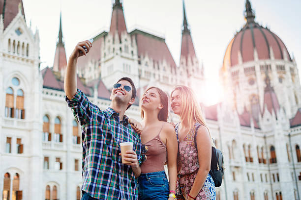 Couple or group of young friends sightseeing Budapest, Hungary, exploring its famous landmarks and having fun on sunny summer day. Images taken near Danube river bank in Budapest, near Lanchid (Chain Bridge) and parliament.