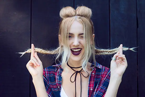 Close up of beautiful young woman with strong dark makeup and purple lips and big smile. Professional modern stylish fashionable hairstyle. Created from small and large braids and loose hair also.