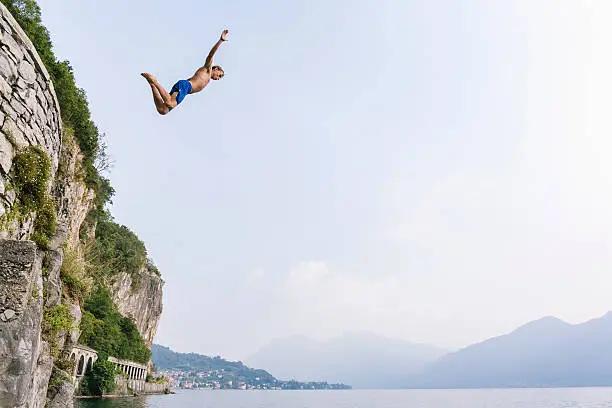 Photo of Brave man diving in the water from a cliff.