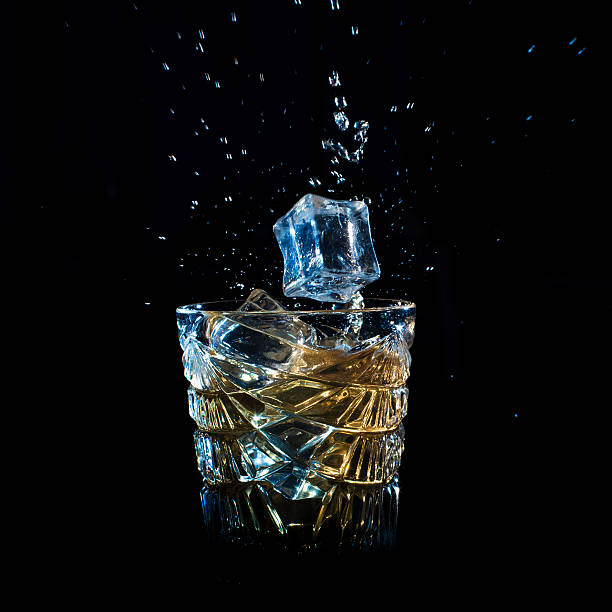 istock Whiskey with ice falling into glass solated on black 603270154