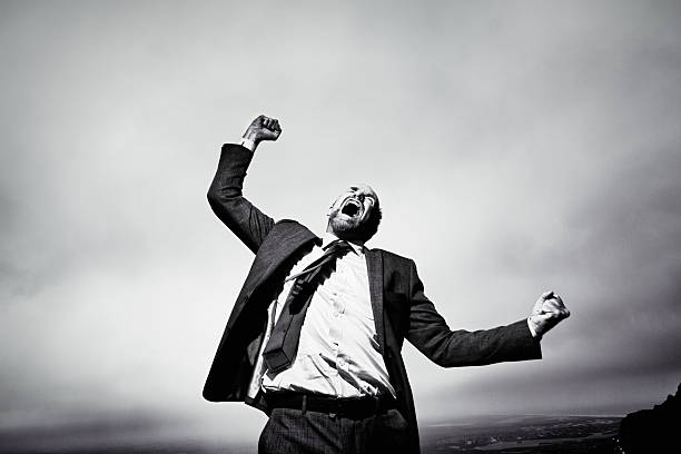 hombre de negocios furioso y frustrado gritando y gesticulando desafiantemente contra el cielo tormentoso - shaking fist fotografías e imágenes de stock