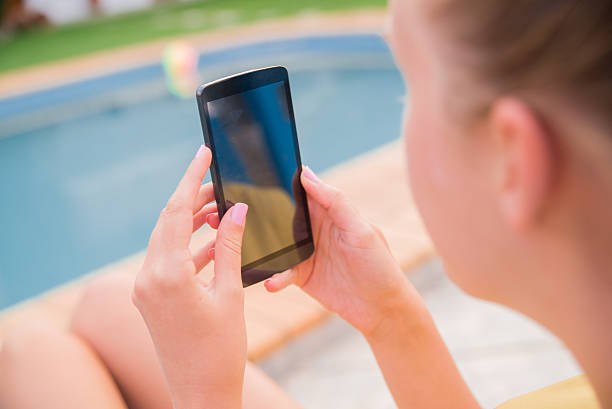 istock Photo of woman using her phone while sitting at poolside 603271782