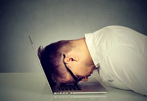 Desperate employee, stressed young man resting head on laptop keyboard