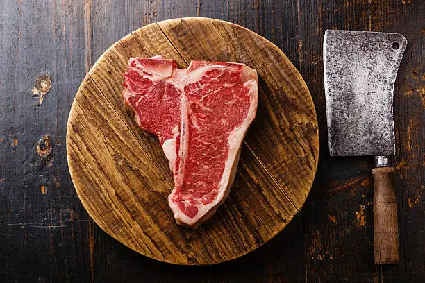 Raw fresh meat T-bone steak and Butcher cleaver on chopping cutting board on wooden background