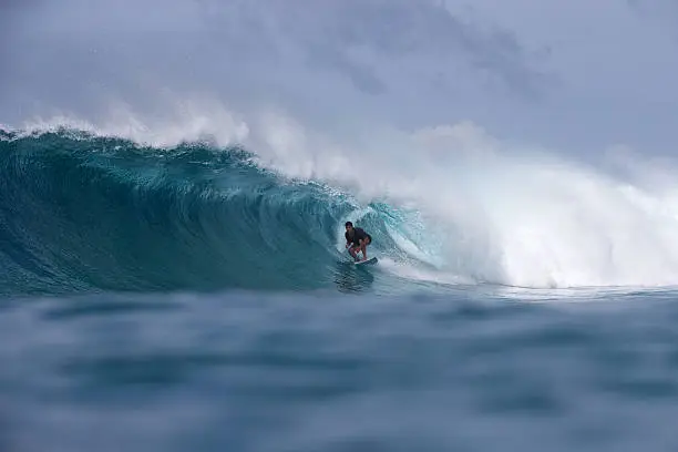 Surfer gets barrelled on a turquoise offshore wave.