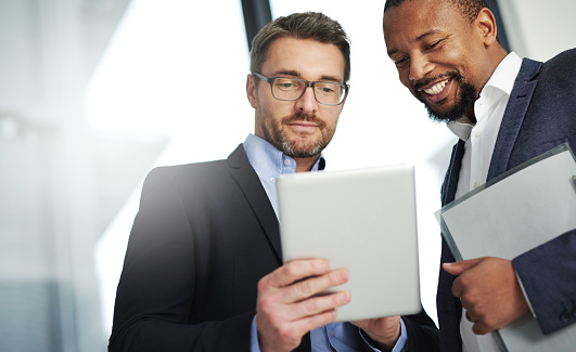 Shot of two businessmen using a digital tablet together at work