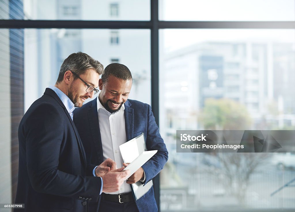 Improving professional performance with the latest apps Shot of two businessmen using a digital tablet together at work Businessman Stock Photo