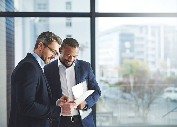 Improving professional performance with the latest apps Shot of two businessmen using a digital tablet together at work business success stock pictures, royalty-free photos & images