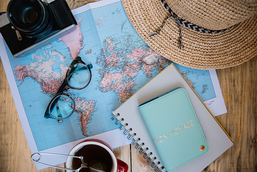 Travel preparations essentials. World map, cup of tea, vintage film camera, hat, passport, notebook and stylish glasses on the old rustic wooden table background, flat lay