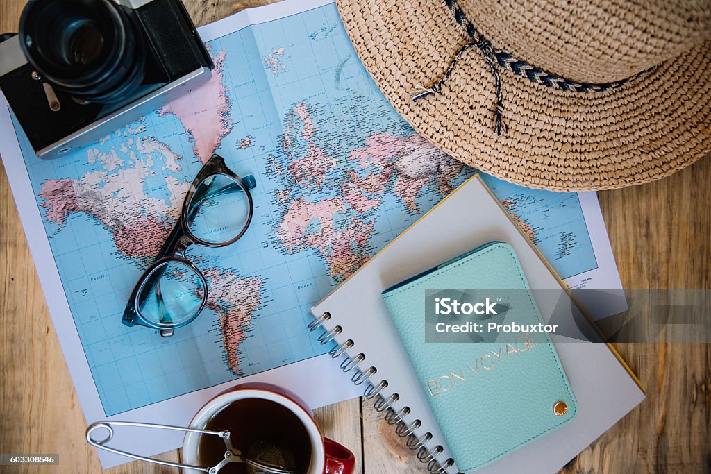 Travel preparations essentials. Travel preparations essentials. World map, cup of tea, vintage film camera, hat, passport, notebook and stylish glasses on the old rustic wooden table background, flat lay Travel Stock Photo