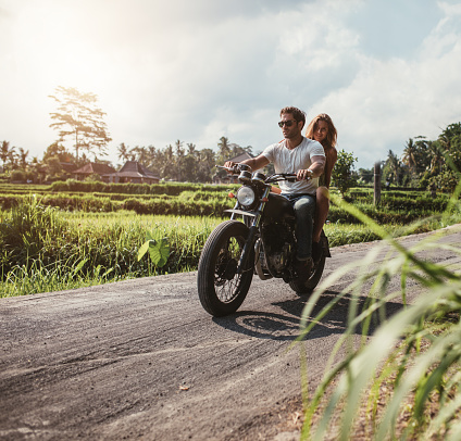 Outdoor shot of couple on motorbike driving through country road. Man and woman riding motorcycle on a countryside road.