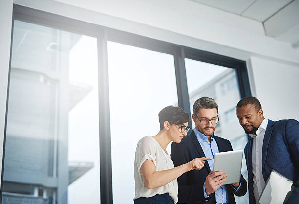 Three departments working towards one goal Shot of a team of colleagues using a digital tablet together at work three people stock pictures, royalty-free photos & images